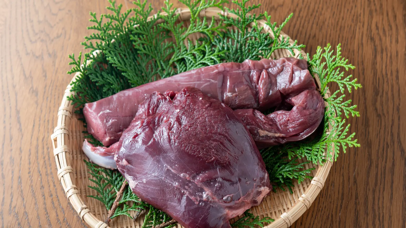 Frisches rohes Wildbret, Rücken und Keulenstück, auf einem Korb mit grünen Zweigen