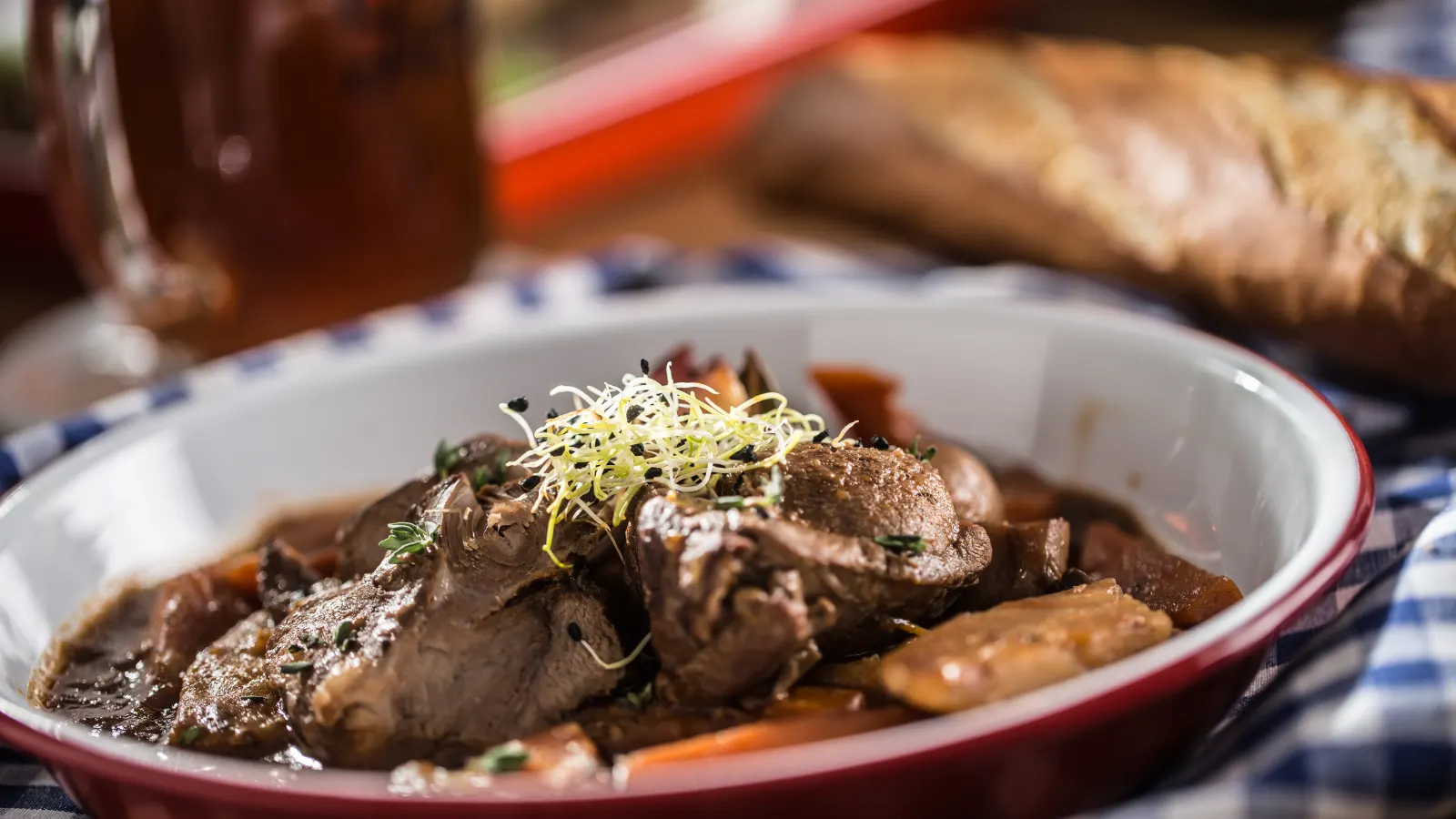 Wildschwein Rezept: Wildschweinkeule aus dem Ofen Geschmorter Wildschweinbraten mit Pilzen und Soße in einer Auflaufform, daneben Brot